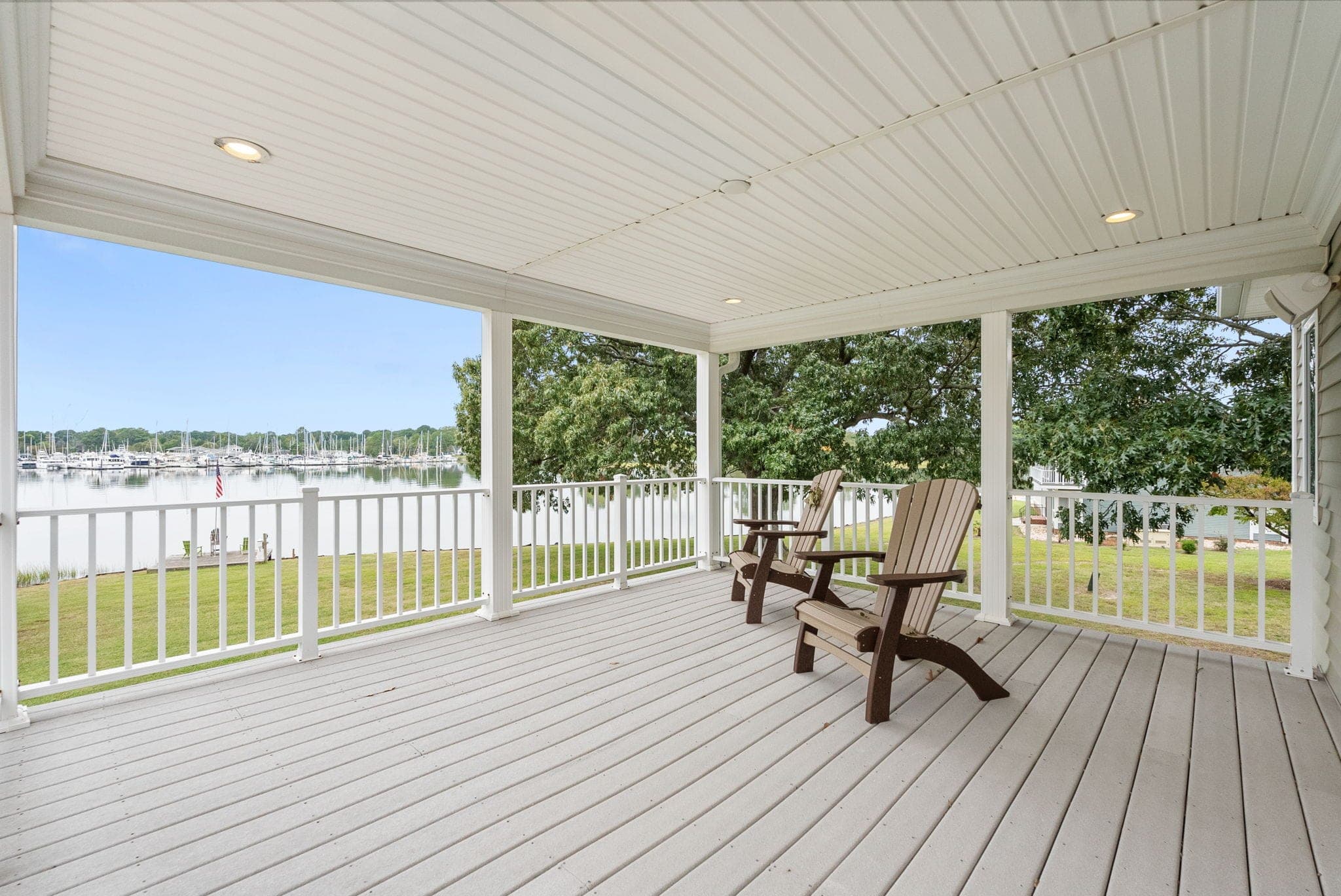 The primary suite's covered balcony: Adirondack chairs, the lawn, and the boats across the creek.
