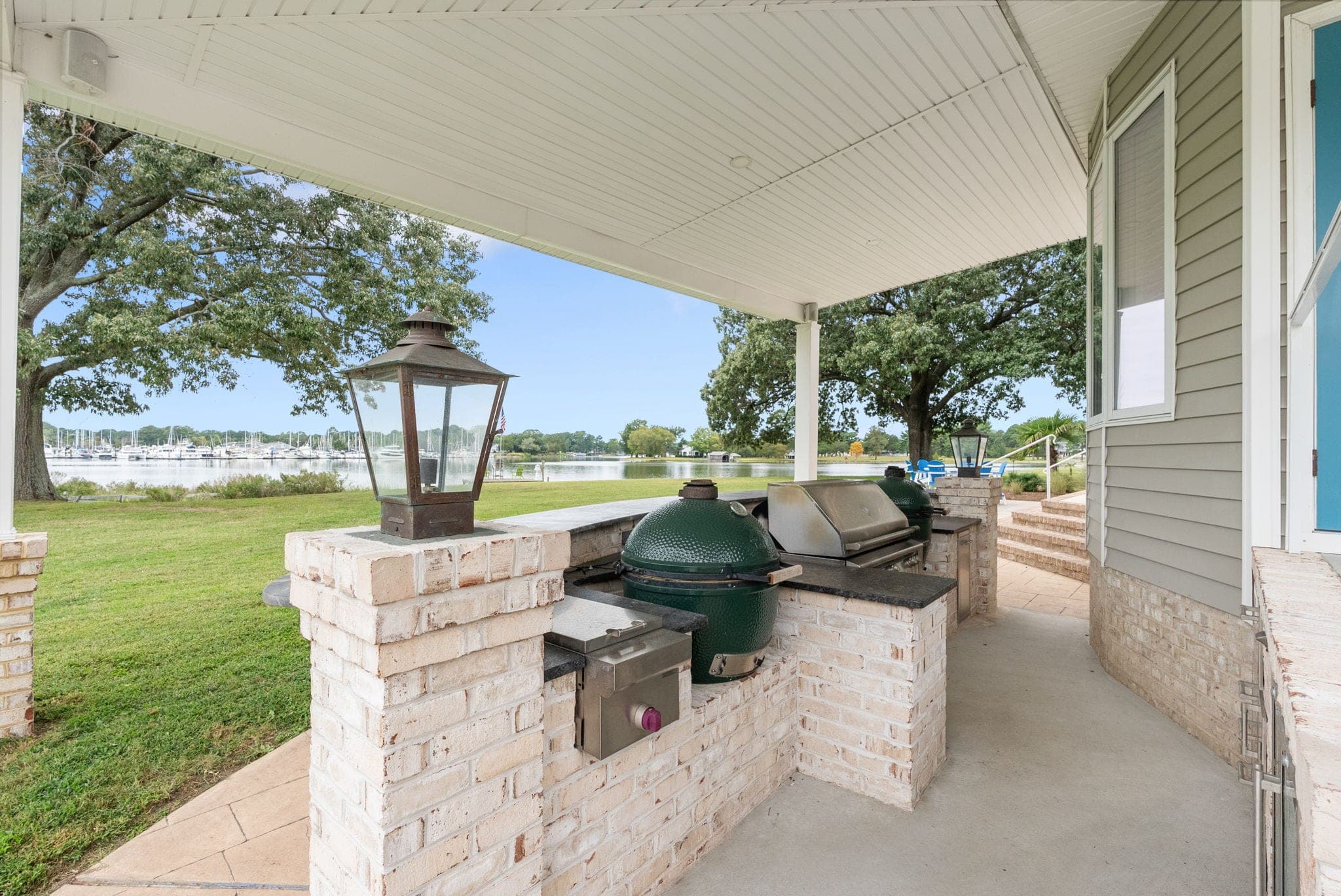 The full outdoor kitchen under the covered patio, with propane sconces, a grill, and a kamado smoker set in brick.